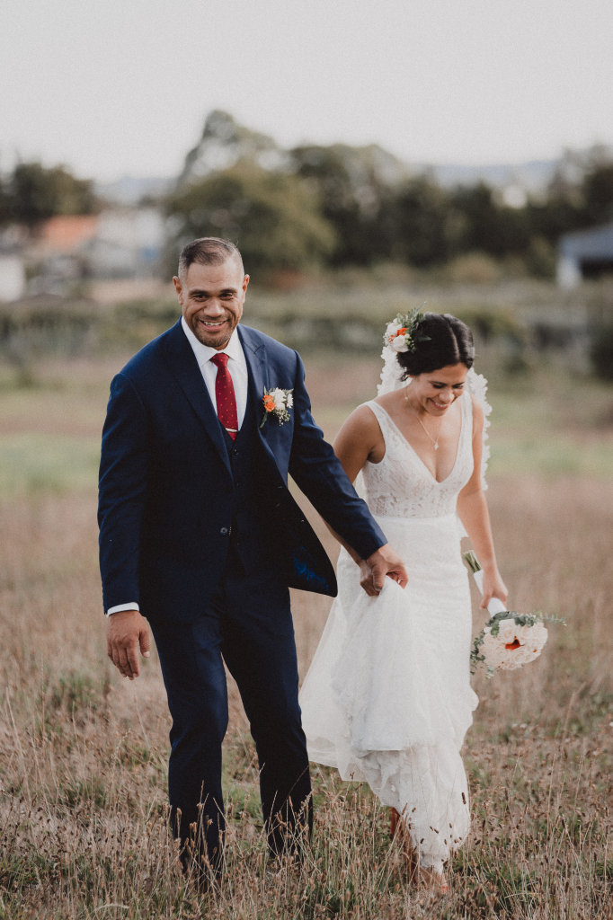 bride and groom walking together in the long grass holding hands